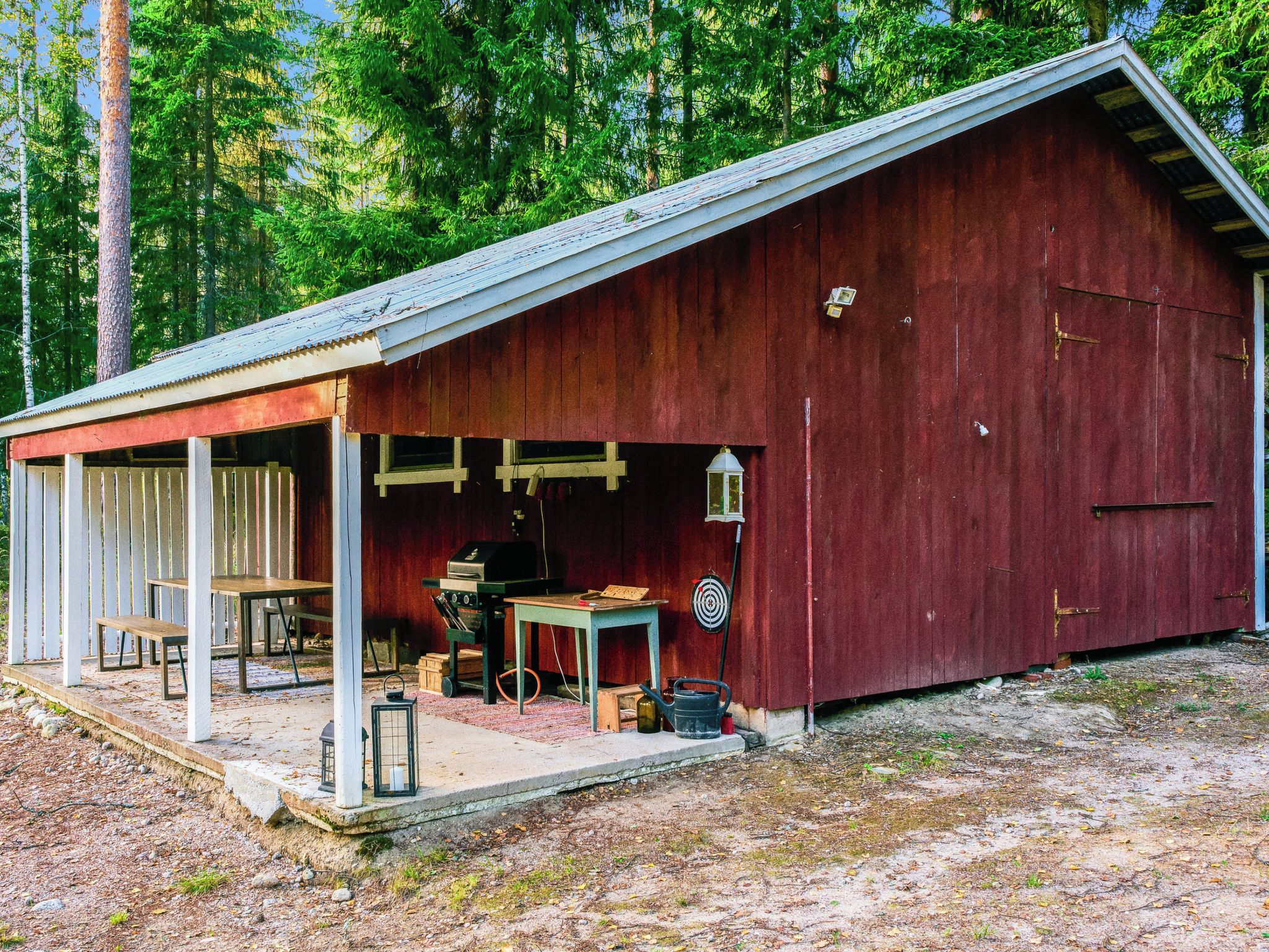 A rustic wooden barn with a covered porch, a table, chairs, a grill, and a lantern.
