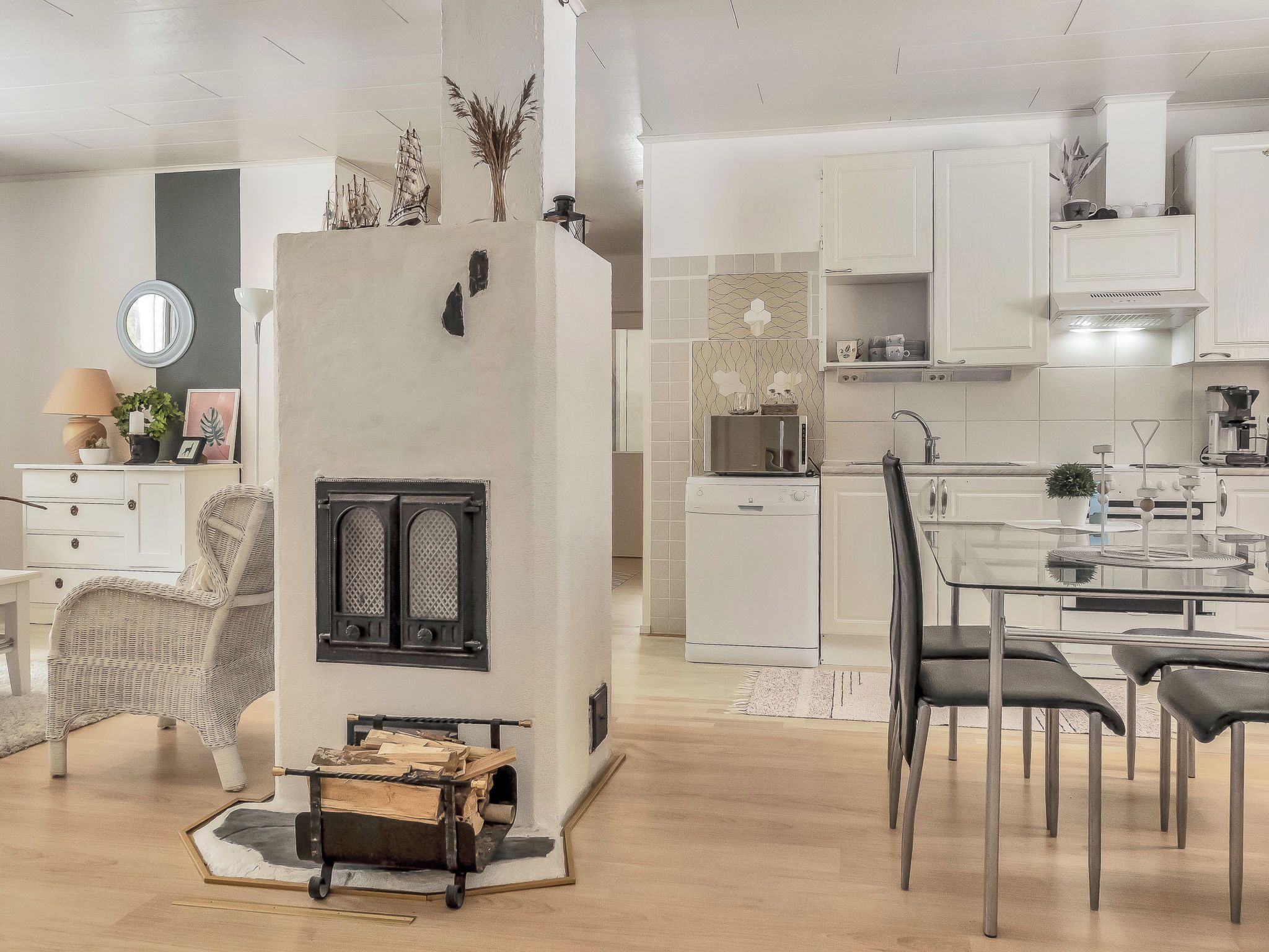 A modern kitchen with white cabinetry, a dining area with a glass table, and a fireplace with a decorative mantel.