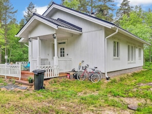 A white single-story house with a porch, a bicycle, and a trash bin.
