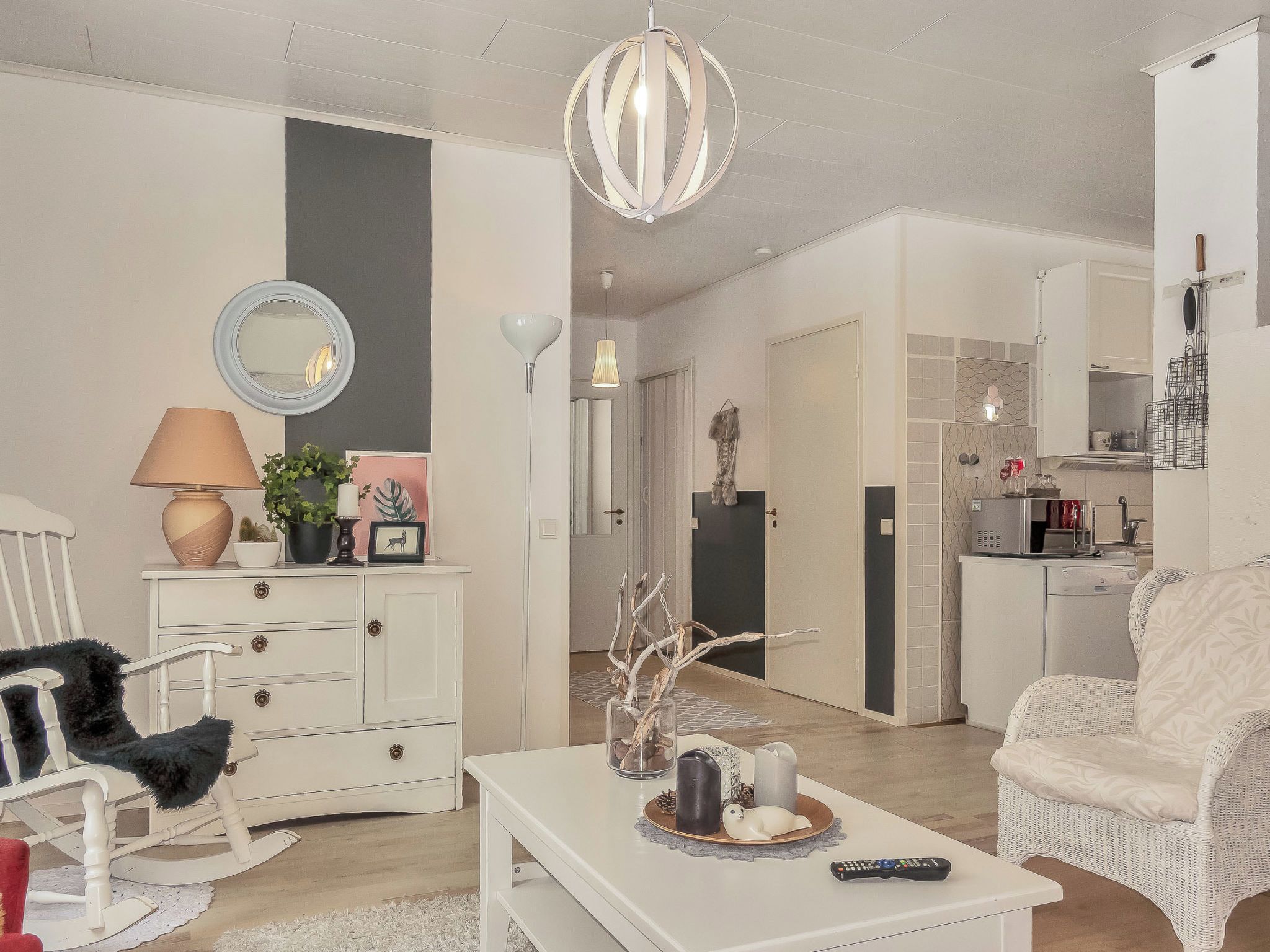 Una sala de estar con un sofá blanco, una mesa de centro blanca con objetos decorativos, un aparador blanco y un espejo.