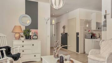 Una sala de estar con un sofá blanco, una mesa de centro blanca con objetos decorativos, un aparador blanco y un espejo.