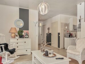 Una sala de estar con un sofá blanco, una mesa de centro blanca con objetos decorativos, un aparador blanco y un espejo.