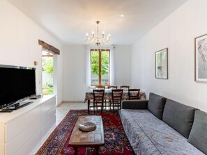 Ein Wohnzimmer mit Fernseher, Sofa, Esstisch und Stühlen.