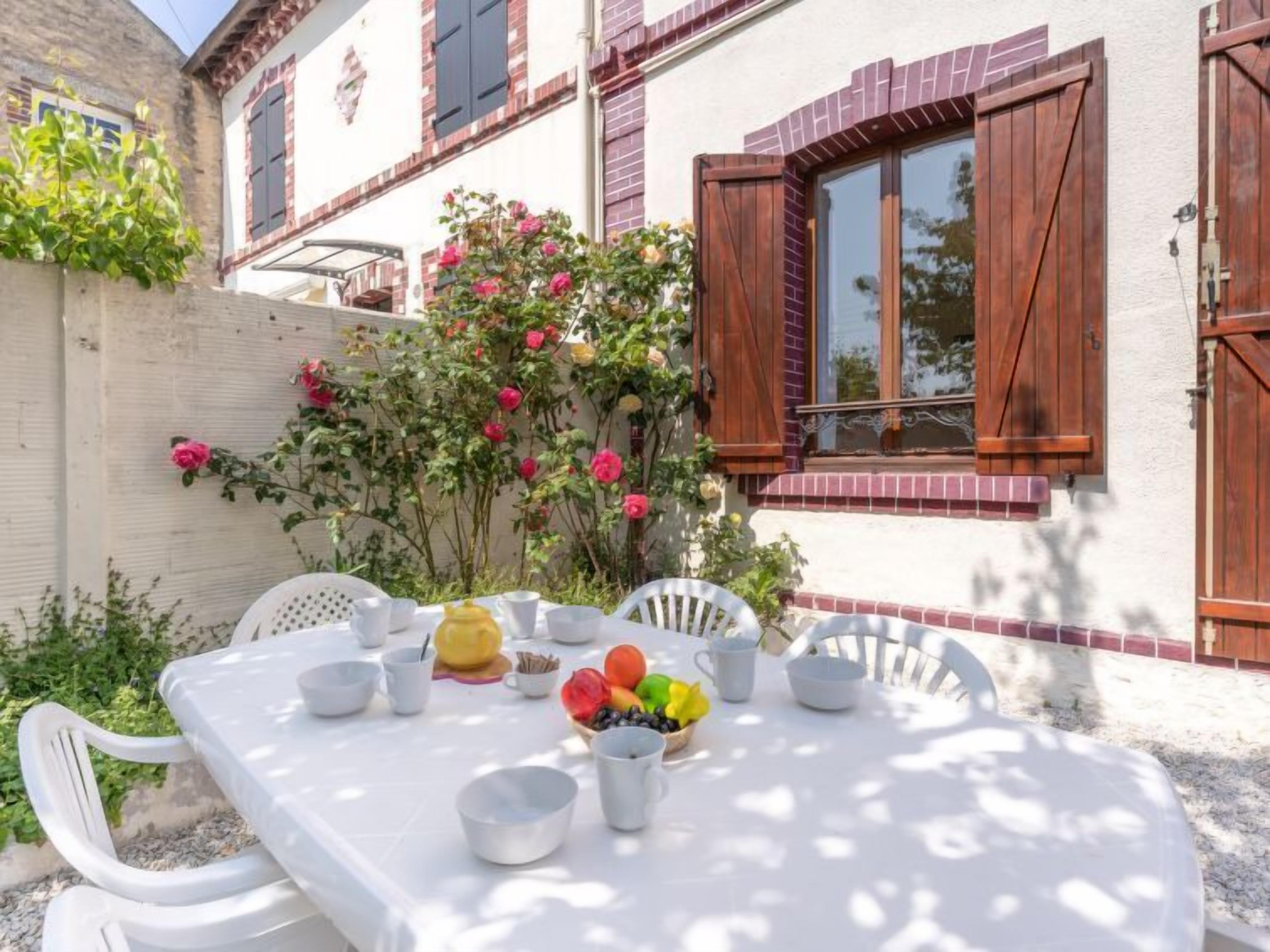 Una mesa al aire libre con sillas, un frutero y un mantel blanco.