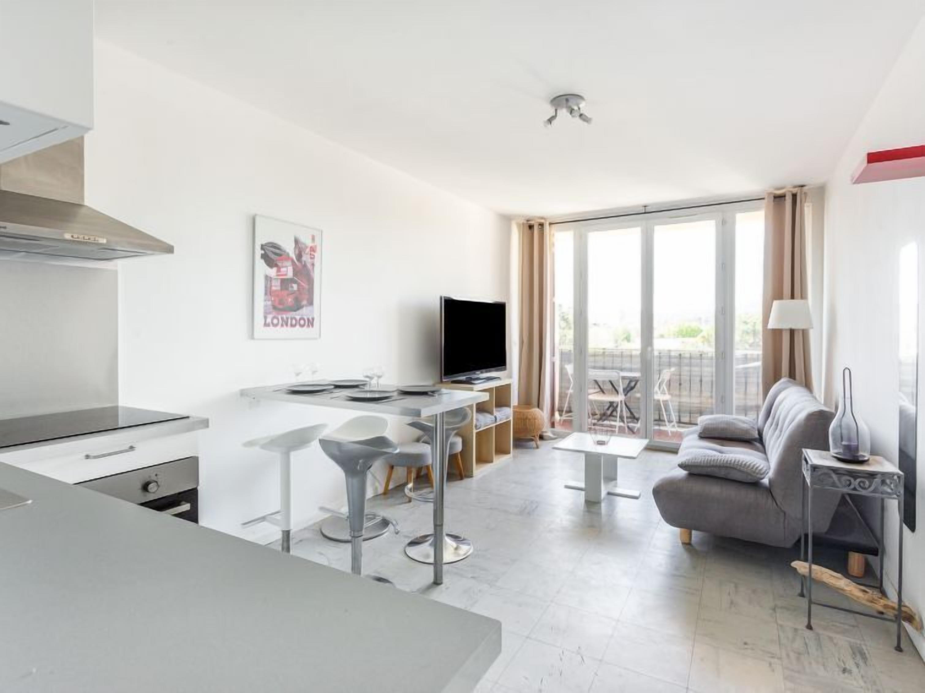 A modern apartment with a kitchen, dining area, and living room. It includes a flat-screen TV, a sofa, and a balcony with a view.