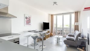 En moderne lejlighed med et køkken, spiseområde og opholdsstue. Der er et fladskærms-tv, en sofa og en balkon med udsigt.