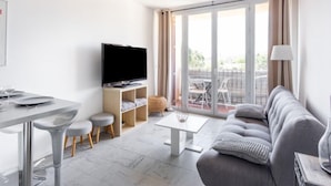 En moderne stue med et fladskærms-TV, et spiseområde med bord og stole, en sofa og en balkon med udsigt.