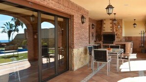 An outdoor patio with a brick fireplace, glass doors leading to a pool, and outdoor furniture. - El balcón de la cala by Interhome (Rincón de la Victoria)