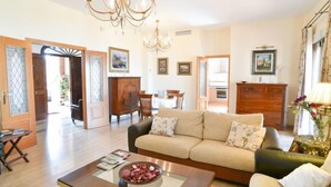 A spacious living room with a sofa, coffee table, and chandelier. There are wooden doors and a dining area visible in the background. - El balcón de la cala by Interhome (Rincón de la Victoria)
