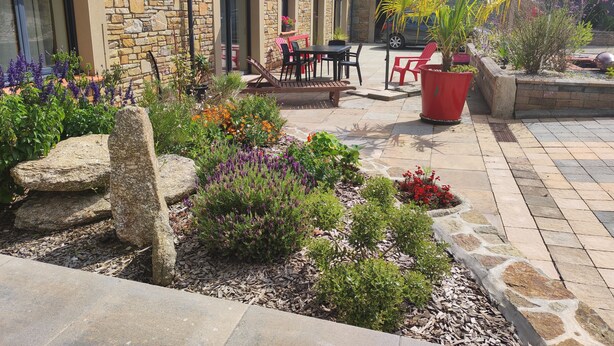 A stone building with a patio area featuring outdoor seating, a potted plant, and a variety of flowers. - The deer house (Plouigneau)