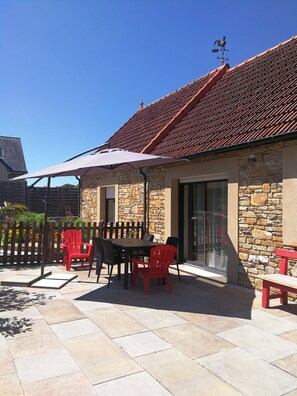 A patio area with a stone wall, a tiled roof, and a table with chairs. - The Deer House (Plouigneau)