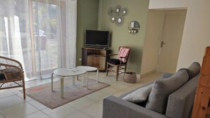 A living room with a grey sofa, a small round table, a wicker chair, a television on a stand, and a sliding glass door. - The deer house (Plouigneau)