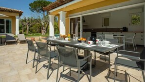 Uma área de refeições ao ar livre com mesa e cadeiras, uma cozinha ao fundo e céu claro.