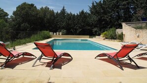 Piscina retangular com um deck ladrilhado, rodeada por espreguiçadeiras vermelhas.