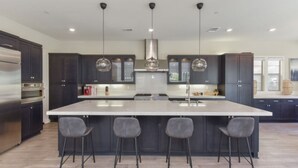 A modern kitchen with dark cabinetry, a large island with bar stools, and pendant lighting.