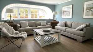 A living room with a beige sofa, a white armchair, a coffee table, and a lamp. There is a window with curtains and a picture frame on the wall. - Tasteful vacation apartment with great attention to detail (Juist)