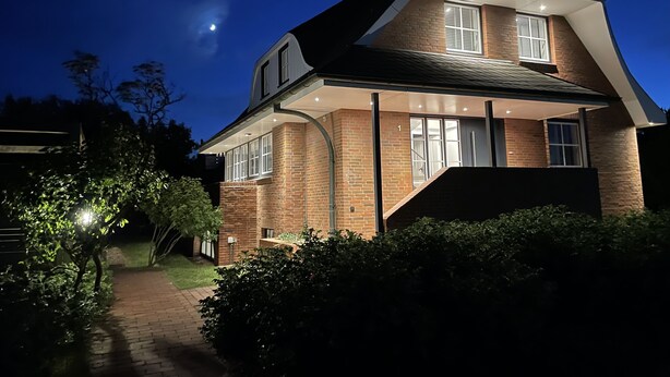 A two-story house with a brick facade, a covered porch, and a visible staircase leading to the upper floor. - Tasteful vacation apartment with great attention to detail (Juist)