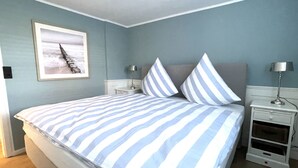 A bedroom with a bed, two nightstands, a lamp, a framed picture on the wall, and a wooden floor. - Tasteful vacation apartment with great attention to detail (Juist)