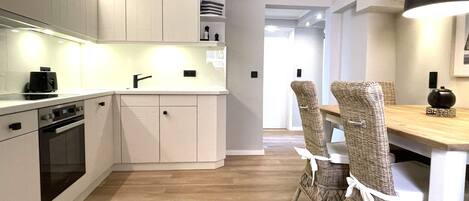 A modern kitchen with white cabinetry, a built-in oven, and a dining area with wicker chairs and a wooden table.