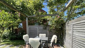 A patio with a wooden table and chairs, surrounded by a wooden fence and greenery. - Tasteful vacation apartment with great attention to detail (Juist)