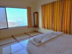A hotel room with a large bed, a window with curtains, a mirror, and a view of the mountains.