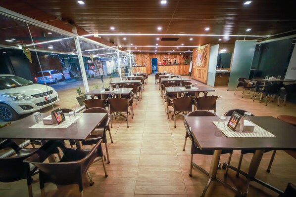 A restaurant with multiple tables and chairs, a wooden ceiling, and a car parked outside.