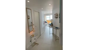 A modern hallway with a mirror, a small table with a lamp, and a view into a living area. - L'HORIZON -Apartment 1st line sea view Class3* (Palavas-les-Flots)
