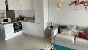 A modern living space with a kitchen, a sofa, and a coffee table. - L'HORIZON -Apartment 1st line sea view Class3* (Palavas-les-Flots)