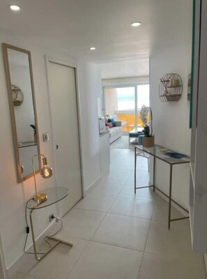 A modern hallway with a mirror, a small table with a lamp, and a view into a living area.