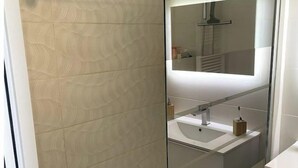 A modern bathroom with a glass shower enclosure, a large mirror, and a white sink. - L'HORIZON -Apartment 1st line sea view Class3* (Palavas-les-Flots)