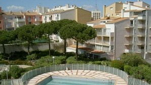 Zona residencial con piscina rodeada de vegetación, una cerca y edificios de varios pisos al fondo.