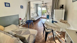 Un espacio habitable compacto con sofá, mesa de comedor, ventilador de techo y kitchenette.