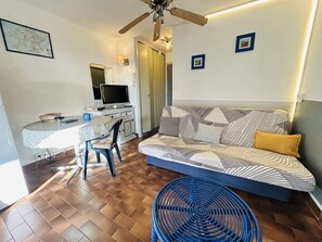 Un espacio habitable compacto con sofá, una mesa de comedor, televisor y ventilador de techo.