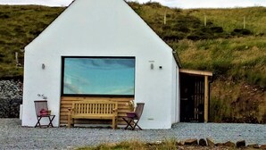 A white building with a large window and a wooden bench outside. - Croft 7 Geary Self Catering Studio (Waternish)