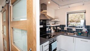 A modern kitchen with white cabinets, a black countertop, and a stainless steel sink. - Croft 7 Geary Self Catering Studio (Waternish)