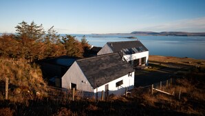 A coastal house with a sloped roof, a fenced yard, and a view of the sea and distant islands. - Croft 7 Geary Self Catering Studio (Waternish)