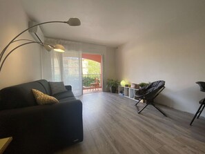 Een moderne woonkamer met een zwarte bank, een vloerlamp, een balkon met een tafel en stoelen, en een potplant.