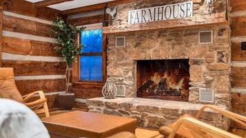 A rustic interior with a stone fireplace labeled "FARMHOUSE," wooden furniture, and a large window with a view.