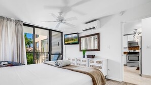 Un dormitorio con una cama grande, un ventilador de techo, un televisor y vistas al exterior.