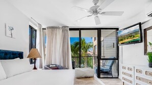 Habitación de hotel moderna con una cama grande, ventilador de techo, vistas al exterior y un balcón con una silla.