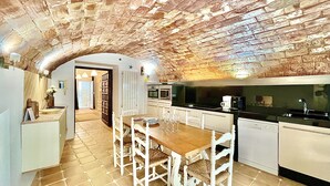 A rustic kitchen with exposed brick walls, a wooden dining table with white chairs, and a modern kitchen counter.
