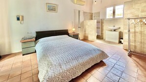 A bedroom with a large bed, bedside tables, a wardrobe, and a bathroom with a sink and mirror.