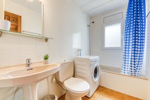A bathroom with a sink, toilet, washing machine, and a shower with a polka dot curtain. - LES TEULES 3A Roses (Rosas / Roses)