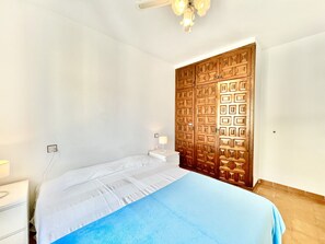 A bedroom with a bed, a nightstand, a lamp, and a wooden wardrobe. - LES TEULES 3A Roses (Rosas / Roses)