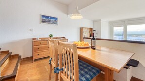 A dining area with a wooden table, chairs, and a view of the sea through large windows.