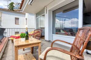 A balcony with a wooden table and wicker chairs, a bottle of champagne, and a glass. - LES TEULES 3A Roses (Rosas / Roses)