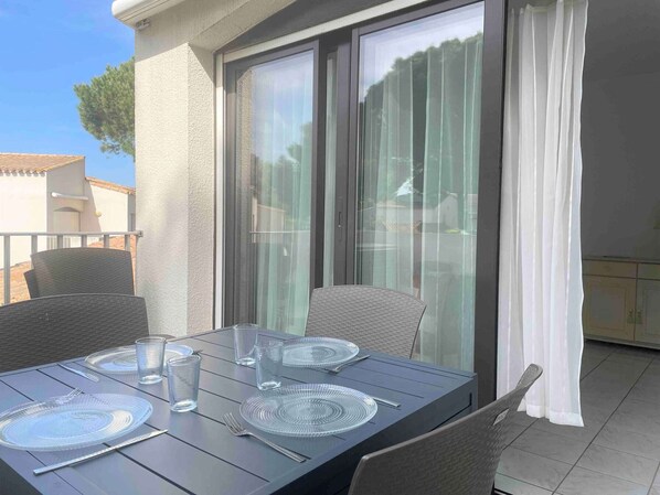 A dining table set with plates, cutlery, and glasses on an outdoor patio with a view through a sliding glass door.