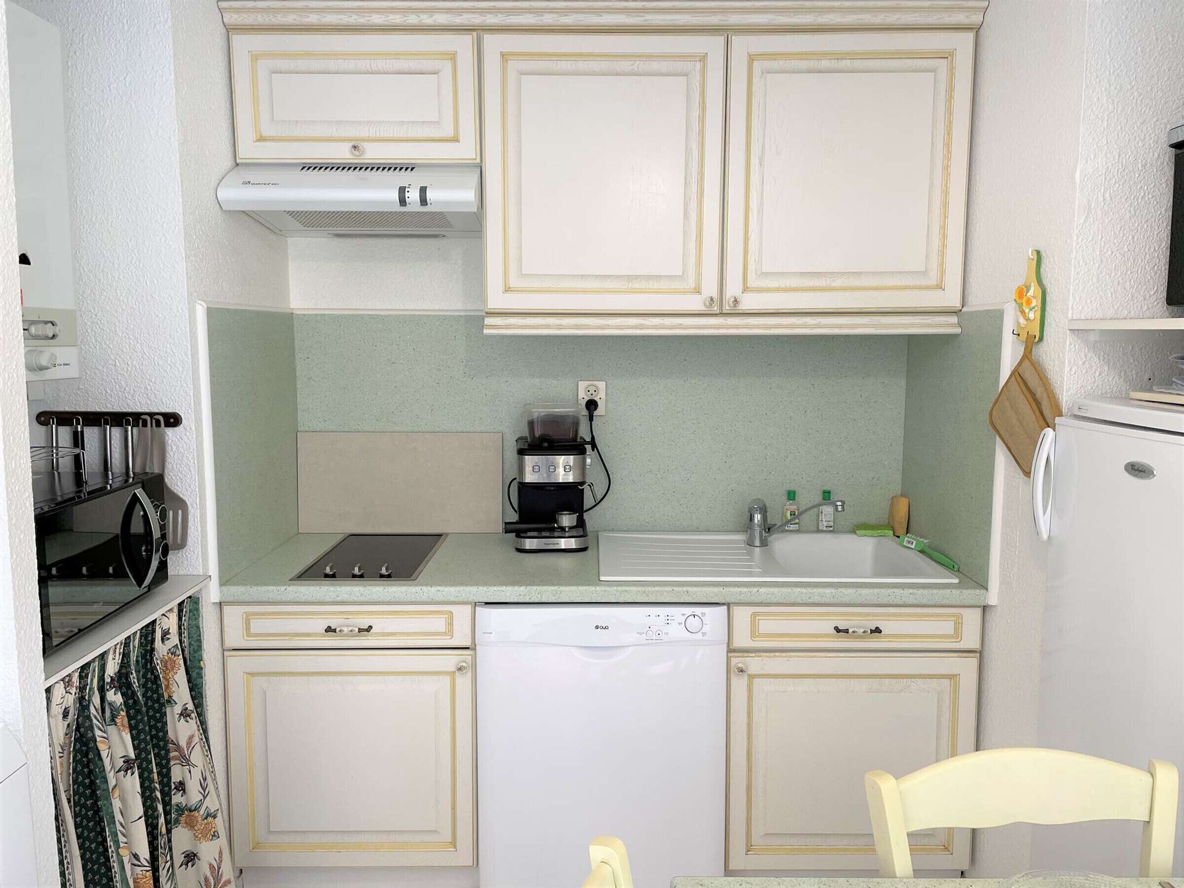 A compact kitchen with a stove, coffee maker, dishwasher, and a small refrigerator.