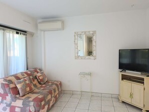 A living room with a sofa, a television, a cabinet, and a mirror. - Beachside Apartment with Pool, Tennis, Parking & Terrace - Sleeps 6 (Cap d'Agde)