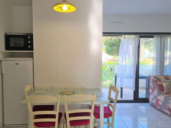 A small dining area with a table and chairs, a microwave, a refrigerator, and a sliding glass door leading to an outdoor area.